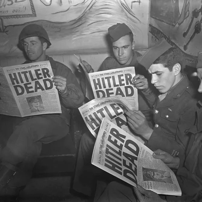 A black and white historical photograph of three soldiers in uniform reading 'Extra' newspapers from 'The Stars and Stripes' with the headline 'HITLER DEAD'.