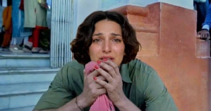 A woman with short dark hair is shown crying emotionally, holding a pink cloth to her face with red-painted nails.
