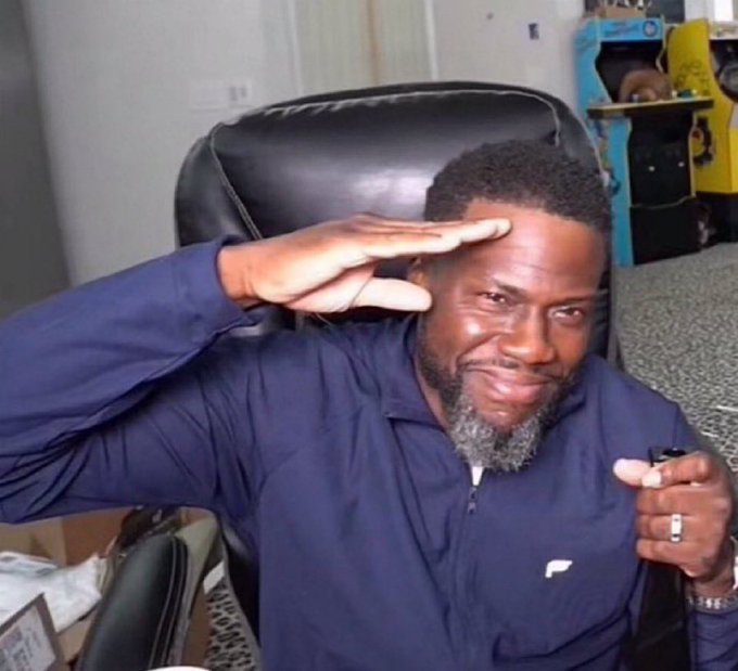 A meme photo of Kevin Hart sitting in a chair, making a hand gesture over his forehead as if shielding his eyes to look into the distance.
