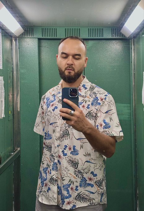 A bearded man takes a mirror selfie in a green elevator, wearing a tropical Hawaiian shirt with blue and red floral patterns while holding up his phone. The image ties to a daily selfie campaign tracking the $chog token, which is currently priced at $0.0016 with a $1.6M market cap as part of a "Day 61" countdown to the $1 price target.