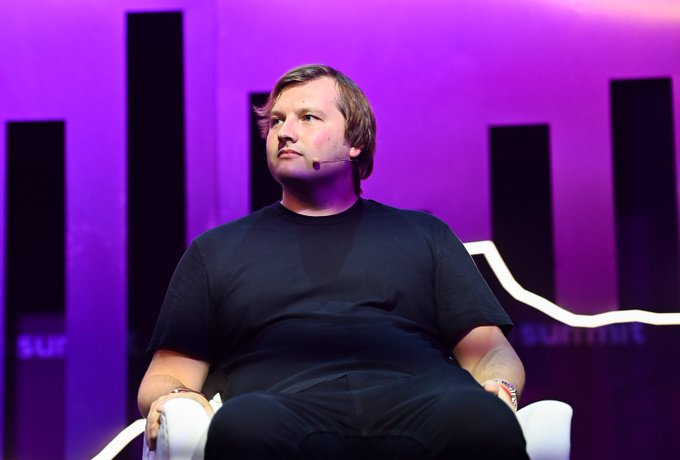 A man with light brown hair, identified as Aave founder Stani Kulechov, sits on a white chair against a purple-lit backdrop featuring the "SUMMIT" logo, as he shares his views on the CLARITY Act's potential to expand crypto's total addressable market.