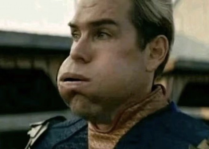 A close-up shot of a man with light brown hair wearing a blue shirt over a peach turtleneck, looking off-camera with a confused expression.