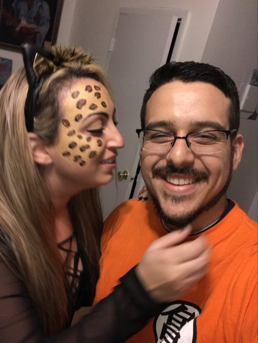 A man in an orange Dragon Ball shirt and glasses smiles next to a woman in leopard print costume makeup and cat ears.
