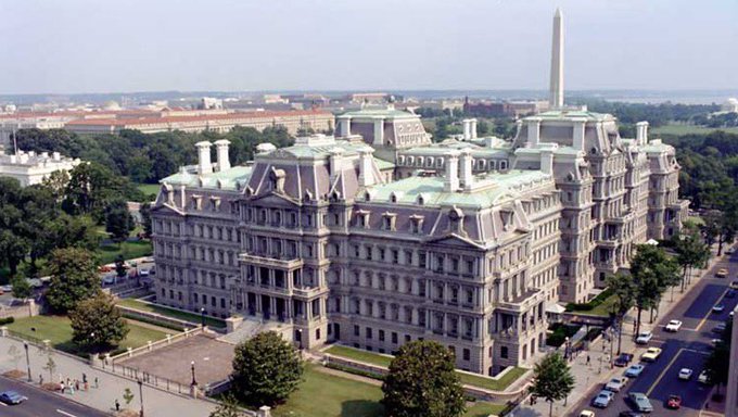 An aerial photograph of the Eisenhower Executive Office Building (EOP) next to the White House in Washington, D.C., with the Washington Monument visible in the background.