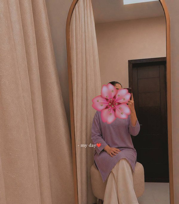 A person wearing a lavender dress takes a mirror selfie with a pink flower emoji covering their face, captioned "my day ❤️" as they sit in a cozy room, complementing the optimistic and grounded mindset of the post about starting the new week with positive energy and manifesting crypto gains.