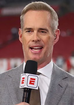 A sports broadcaster with short blonde hair, wearing a gray suit, speaks into a microphone featuring the ESPN logo.