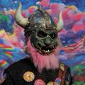 An illustration of a warrior character wearing a horned helmet with a pink beard, set against a colorful, abstract background.