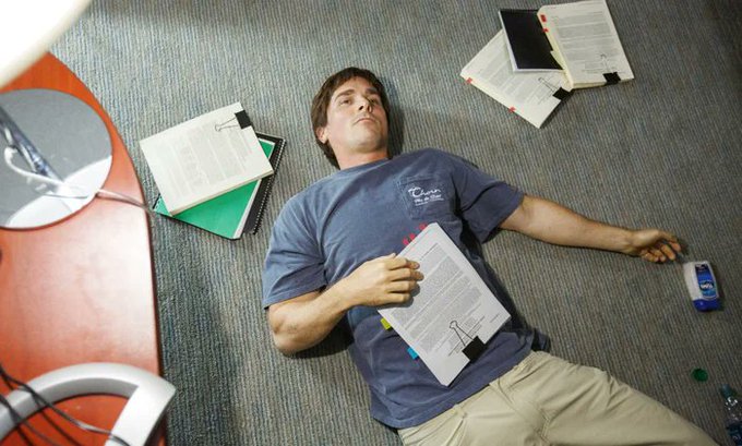 A young man lies sprawled on the office carpet, exhausted from studying, with binders, loose papers, and a juice carton scattered around him—capturing the "happy weekend" mood of being completely burned out and ready to call it a week.