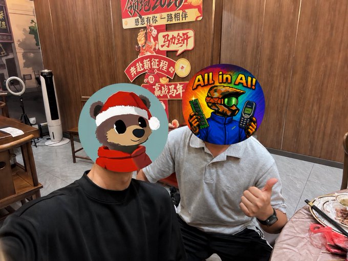 Two people pose for a photo at a restaurant decorated with Chinese New Year banners reading "领跑2026" (Leading 2026), "感恩有你一路相伴" (Grateful for your company along the way), and "奔赴新征程 赢战马年" (Rushing toward a new journey, winning the Year of the Horse), with their faces playfully covered by cartoon stickers — one a festive bear in a Santa hat and the other a colorful "All in AI" robot — suggesting an in-person meetup of the AI-focused online collaborators mentioned in the post.