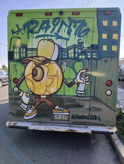 A photograph of a food truck's rear doors featuring colorful graffiti art of a yellow anthropomorphic egg-like character wearing a hat, holding spray cans, with 'ZMF-8244' license plate and @AerosolBon artist signature.