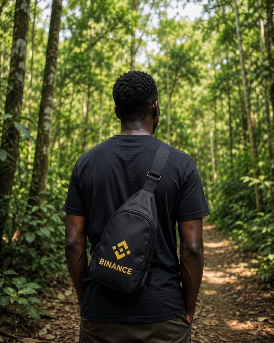 A man walks through a forest carrying a black sling bag with the "Binance" logo. This image complements the "Happy Sunday" message by suggesting a peaceful and natural way to spend the day.