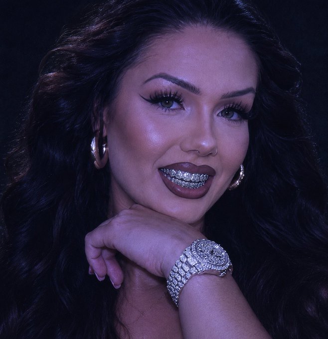 A glamorous woman with long dark wavy hair, dramatic eye makeup, hoop earrings, and a sparkling diamond watch smiles confidently at the camera, her jewel-encrusted grillz prominently displayed. The luxurious styling and confident pose visually amplify the post's bullish sentiment about XRP reaching 4-5 digits, projecting an aura of wealth and success befitting such a price prediction.