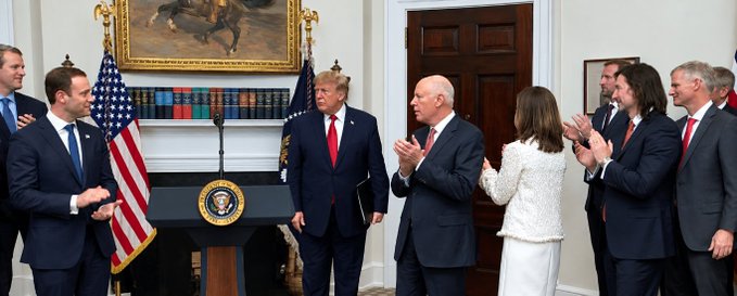 A group photo taken in the White House showing several political figures including Donald Trump standing near the presidential seal podium with an American flag in the background.