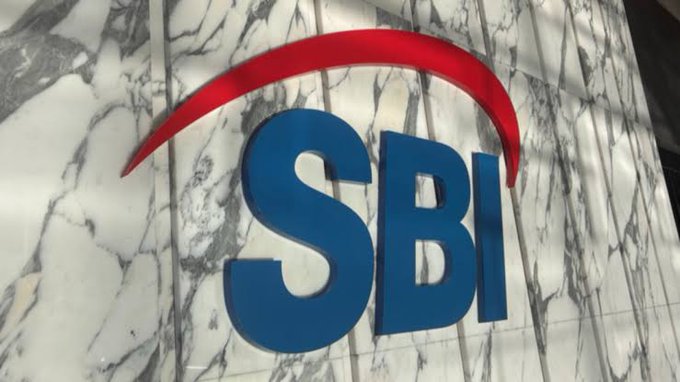 The image shows the SBI logo in blue lettering with a distinctive red arc above it, mounted on a white marble wall. While the post discusses SBI Holdings' partnership with Solana for yen stablecoins and tokenized assets, the logo shown is for SBI (State Bank of India), which is a separate entity from Japan's SBI Holdings.