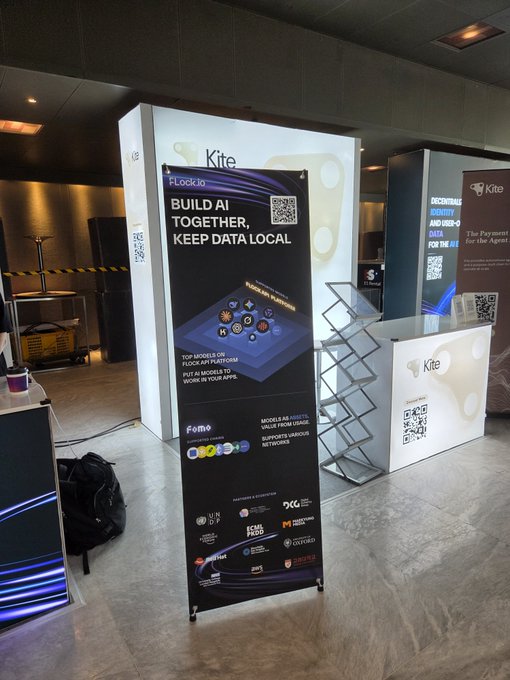A promotional banner for 'Kite' reads 'BUILD AI TOGETHER, KEEP DATA LOCAL' with text mentioning 'Flock.io' and 'Fomo AI', set up at what appears to be a tech conference or event.