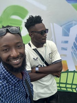 Two smiling men pose together, one wearing a white "Everton" soccer jersey with crossed arms, while the other in a checkered shirt takes the selfie in front of a colorful graphic backdrop. The image accompanies a post tagging @Fettycryptt with hashtags #UnchainSummer26 and @NFT__NG, suggesting the duo is attending a summer NFT/crypto-related event in Nigeria.