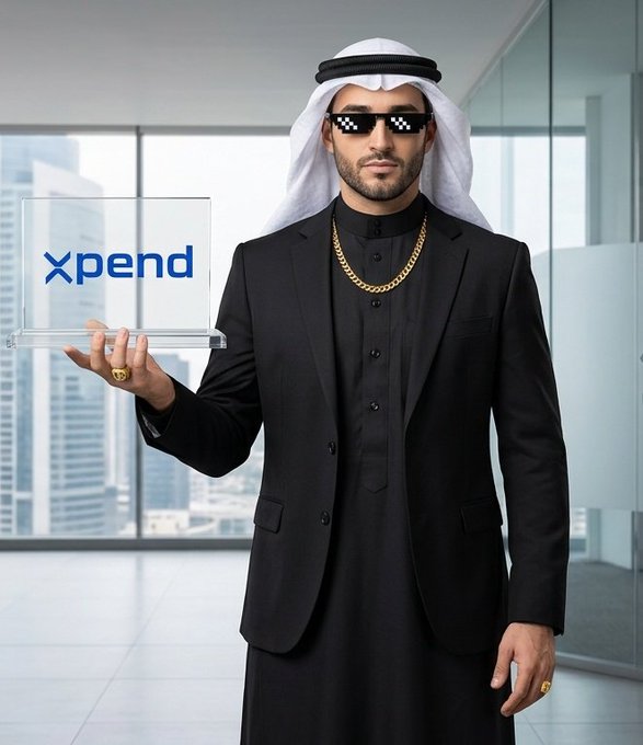 A man wearing a white keffiyeh, black suit, gold chain, and pixelated sunglasses holds a clear acrylic award with the word "Xpend" written on it, set against an office window backdrop.