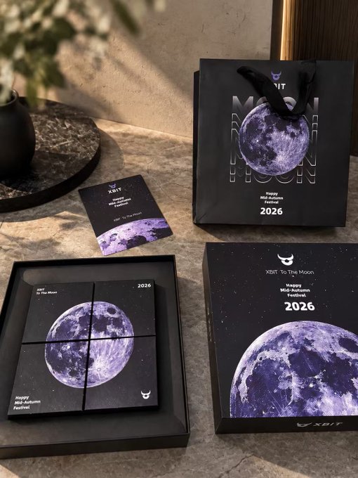 A stylish "XBIT To The Moon" 2026 Happy Mid-Autumn Festival gift set is displayed, featuring a black gift bag, a four-grid mooncake box, and a card—all adorned with purple moon imagery that brings the "feeding from the moon" theme to life in physical form.