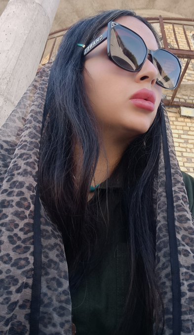 A low-angle selfie of a woman with long dark hair wearing large sunglasses with 'MEXICO' written on the frames and a leopard print scarf.