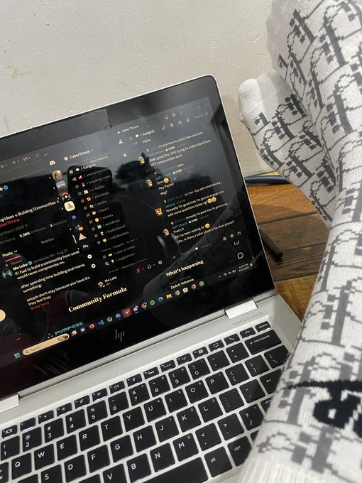 A laptop displaying the Discord application with various servers and messages visible, with feet wearing black and white patterned socks propped up nearby.