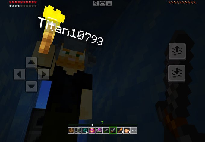 A Minecraft gameplay screenshot showing a character named 'Titsn10793' holding a torch in a dark cave, with mobile control buttons visible on screen.