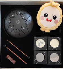 An overhead view of a black tray containing a BTS-themed black makeup palette, an Alpaca plush coin purse, pencils, and four round powder compacts.