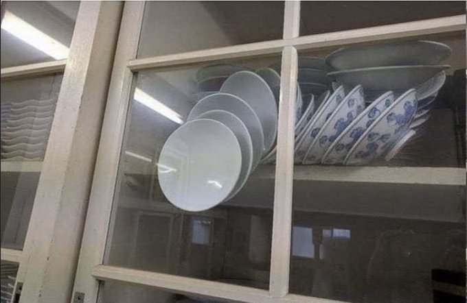 A vintage-style wooden cabinet with glass doors, displaying neatly stacked white and blue-patterned ceramic bowls and plates on its shelves.