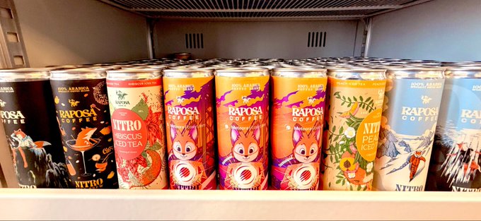 A store shelf displaying various colorful cans of Raposa Coffee, with visible flavors including Hibiscus Iced Tea, Nitro Peach, and a 100% Arabica Nitro option, featuring a fox mascot.