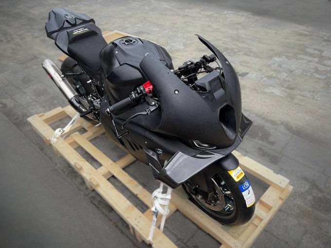 A matte black sport motorcycle secured with white straps on a wooden shipping pallet in what appears to be a warehouse or garage setting.