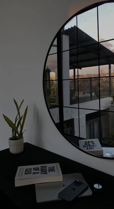 A desk setup features a snake plant, smartphone, and a book titled "CONGRATS ON THE" beside a round window reflecting a cityscape at dusk, evoking the quiet morning victory vibe of the "Only winners can see this. Gm" message.