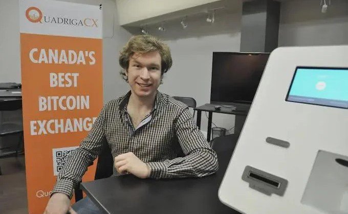 A young man smiling while sitting next to a Bitcoin ATM, with an orange banner behind him reading 'QuadrigaCX - CANADA'S BEST BITCOIN EXCHANGE'.