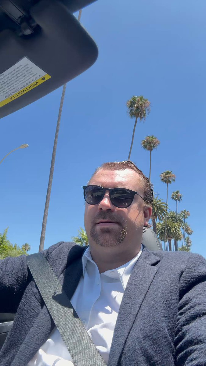iced coffee on a table, with a man wearing sunglasses and a gray suit jacket seated at the table.
