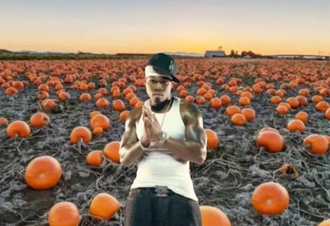 A muscular man in a white tank top stands in a field full of pumpkins at sunset with his hands clasped in a prayer position.