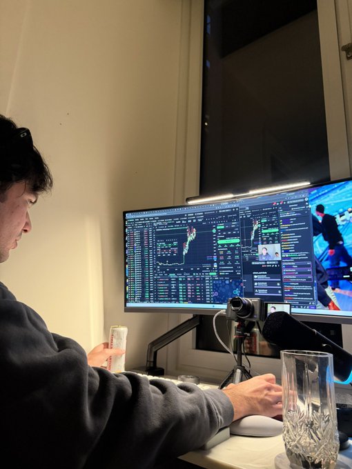 A young man sits at a multi-monitor trading setup with a microphone, a glass, and a beverage can on the desk, while financial charts and data are displayed on the screens in the background—appearing to live stream his copy trading activities on Cented.