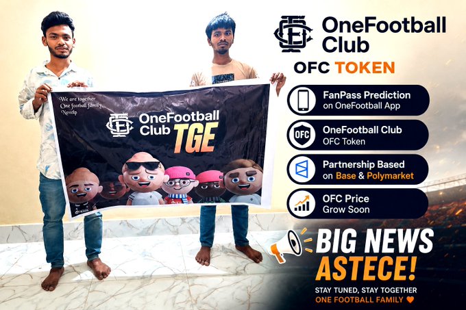 The image features two men holding a large black banner with white text that says "OneFootball Club" and "OFC token". The banner also includes a small cartoon character, possibly representing a football player or mascot. The background of the image is blurred, but there are some people in the scene who appear to be standing around.