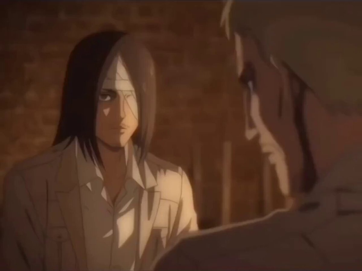 The image shows two people, a man with long hair wearing a white shirt and another person dressed in all white standing next to each other against an orange brick wall backdrop. The man in white has his eyes closed while looking at the other person who is also staring back at him. There are no texts or other objects visible in the image.
