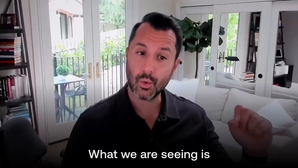 The image shows a man wearing a black shirt sitting in front of a couch with his arms outstretched as if he's giving a speech or making an announcement. The background features a bookshelf filled with various books, suggesting that this might be a living room or a study area. The caption for the image reads: "What we are seeing is @JohnNahas84 is seeing capital moving towards the builders creating new rails, new use cases, and real revenue-generating businesses. That is where Avalanche is focused".