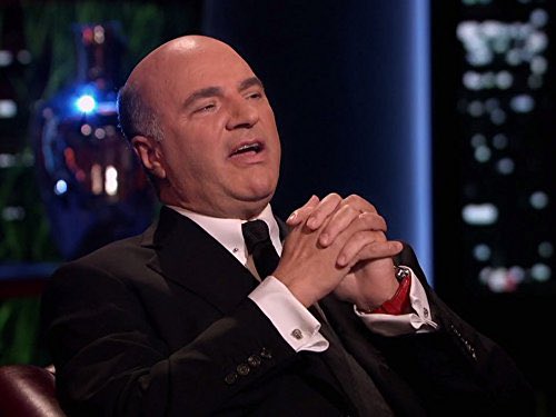 A bald man in a black suit with his hands clasped together, appearing emotional with his eyes closed, shown in what looks like a television studio setting.