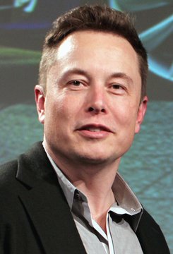 A close-up portrait of Elon Musk wearing a dark blazer over a gray shirt.