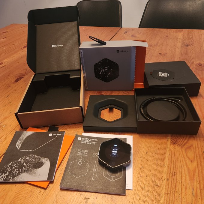 A Bitkey bitcoin hardware wallet unboxed on a wooden table, displaying the hexagonal device, charging cable, and instruction booklet titled "Getting Started: It's Your Money, Not Your Bitcoin," illustrating the collaborative custody concern raised in the caption.