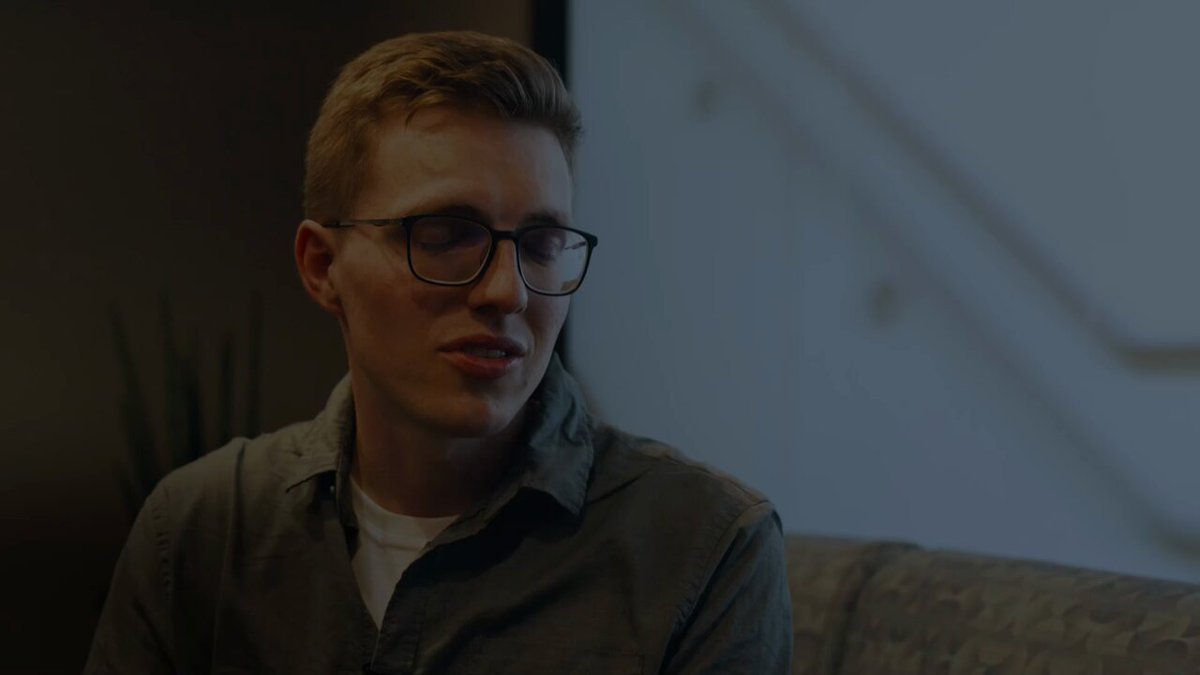 The image features a young man wearing glasses, sitting on a couch with his head tilted back as if he's deep in thought or contemplation. The background of the image is blurred, but there are stairs visible behind him. The caption for this image reads "Cardano can be messy, but it' s exactly what a real decentralized community looks like. This is a community that cares so much it sometimes drives itself crazy. Because what this community needs is a place to move".