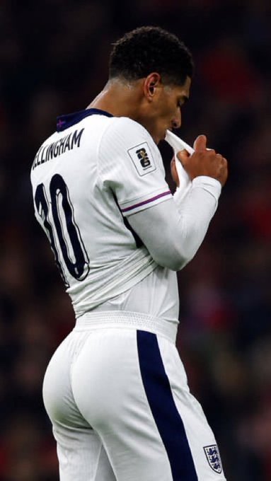 Soccer player Bellingham, wearing the number 30 England kit, kisses the badge on his jersey during a match.