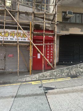 Bamboo scaffolding frames a traditional red door adorned with Chinese characters, while a closed "Gifts" shop and the "天海牛肉店" (Tianhai Beef Shop) sign with the number "247 9180" appear on either side—evoking a hidden "white rabbit" moment in Hong Kong's urban streetscape.