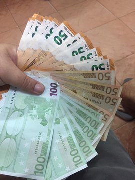A hand fanning out a stack of 50 and 100 Euro banknotes.