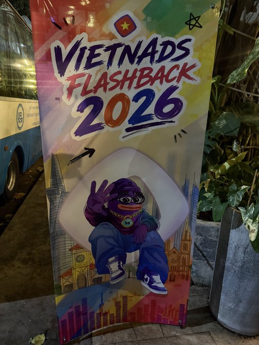 A vibrant banner reads "VIETNADS FLASHBACK 2026" featuring a purple cartoon mascot making a peace sign amid illustrated city skylines and a Vietnamese flag star. The banner promotes the giveaway event, matching the post's announcement of an NFT prize for attendees who follow the specified accounts, post a party photo, and reply with a random number.