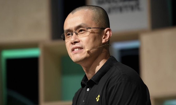 A man with glasses and a short haircut, wearing a black polo shirt with a yellow logo, speaks into a headset microphone, likely during a presentation or talk.