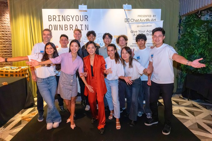 A group of people pose together at an event with a backdrop reading 'BRINGYOUR OWNBRAIN' and 'Presented by ChatAndBuild'.