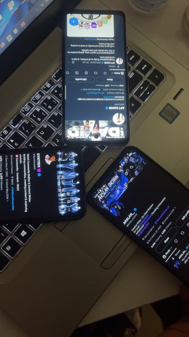 Three smartphones resting on a laptop keyboard, displaying various apps including social media platforms and entertainment content.
