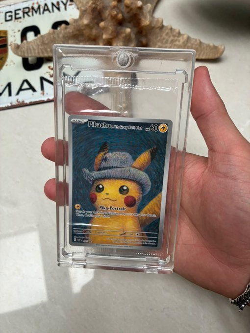 A hand holds a clear protective case displaying a Pikachu Pokémon trading card that resembles Van Gogh's self-portrait, with text reading 'Pikachu with Gray Felt Hat 080' and 'Pika-Portrait'.