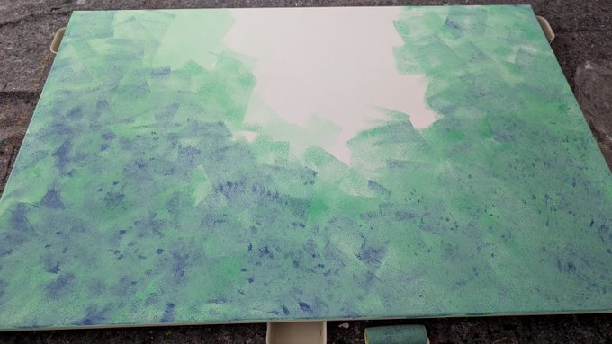 An abstract painting on canvas featuring textured brushstrokes in shades of green and blue, with a central white area resembling a sky or opening, resting on an easel.